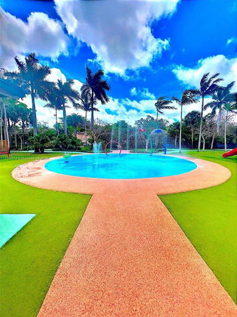 View of an outdoor splash pad with water fountains surrounded by palm trees.
