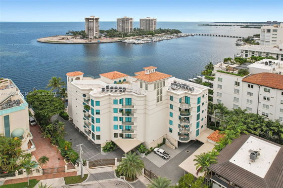 Panoramic view of a waterfront residential building with rooftop features, overlooking a body of water and nearby towers.