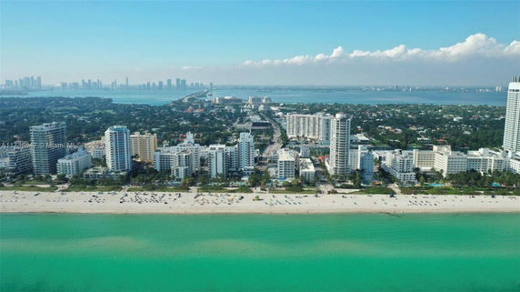 Aerial view of beachfront cityscape with ocean in foreground and skyscrapers in background.