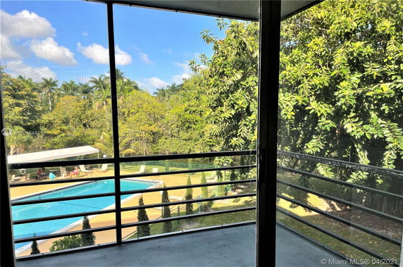 View from a balcony overlooking a swimming pool area surrounded by trees.