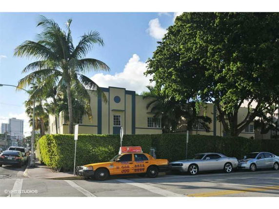 Front view of a two-story building with palm trees and parked cars on the street.