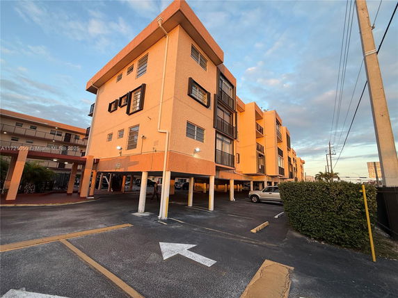 Front view of a multi-story apartment building with covered parking on the ground level.
