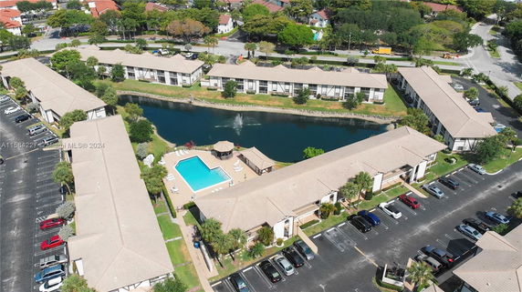 Panoramic view of a residential complex with multiple buildings, a central swimming pool area, and a water feature.
