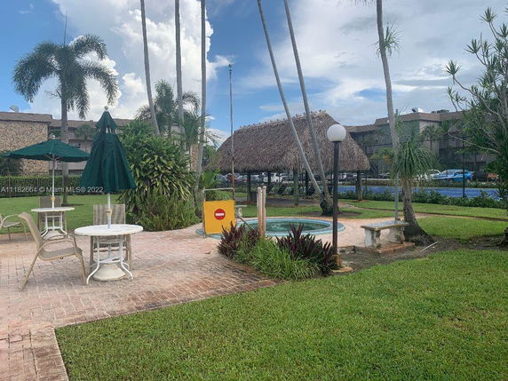 Outdoor recreational area with tables, chairs, umbrella, and a thatched-roof structure.