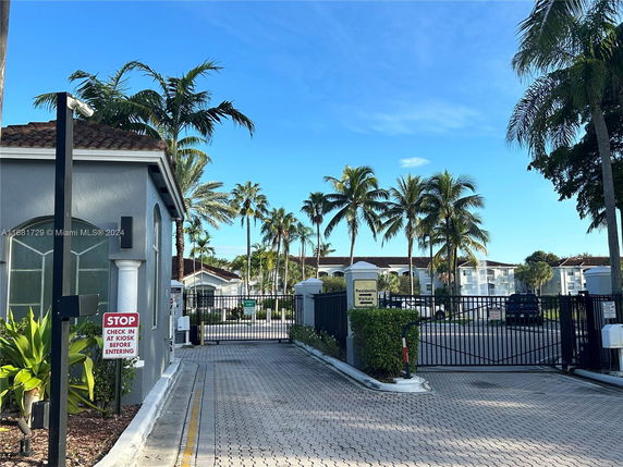 Entrance view of a gated residential area with palm trees and a security kiosk.