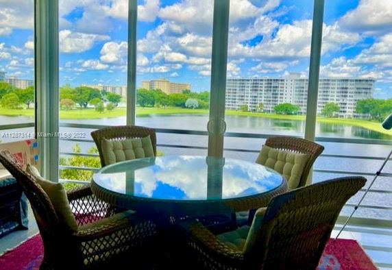 View from a glass-enclosed patio overlooking a lake with buildings in the distance.