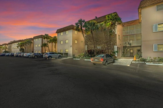 Front view of an apartment building with parking spaces and cars in the foreground.