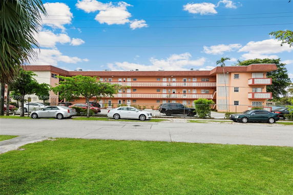 Front view of a multi-story apartment building with balconies and parking area.