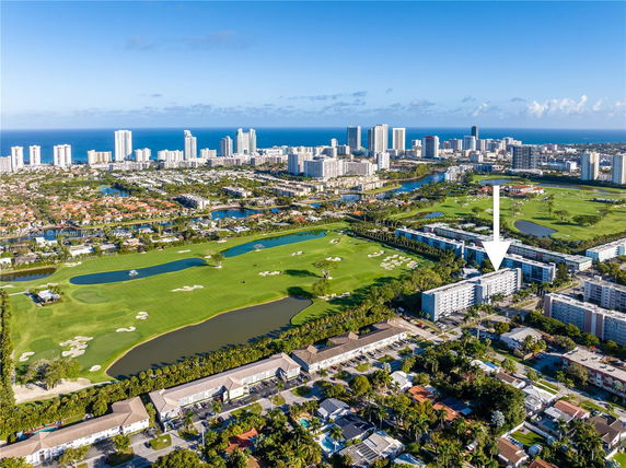 Aerial view of an urban landscape with golf course and high-rise buildings in the background.