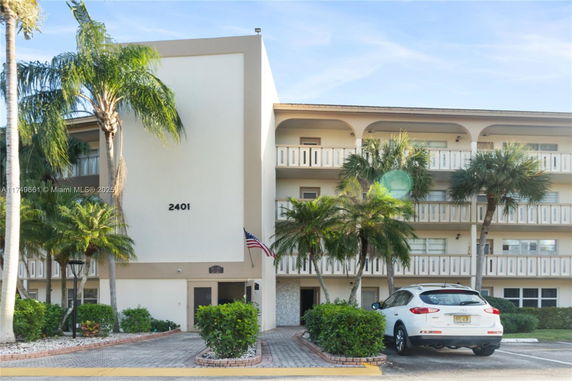 Front view of a multi-story residential building with balconies and palm trees.