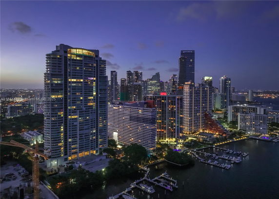 Panoramic view of a city skyline at dusk with illuminated high-rise buildings and waterfront.