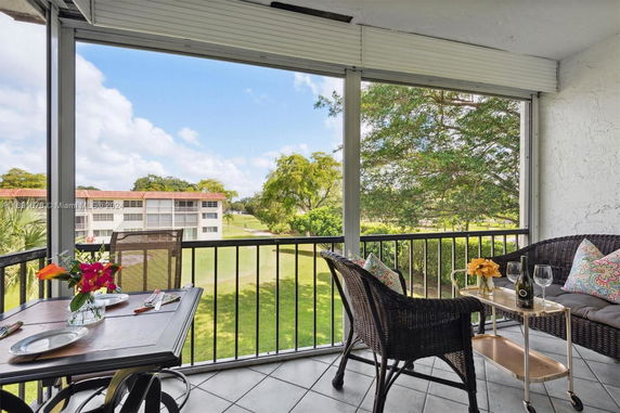 View from a balcony with outdoor seating and a table overlooking a lawn and nearby buildings.