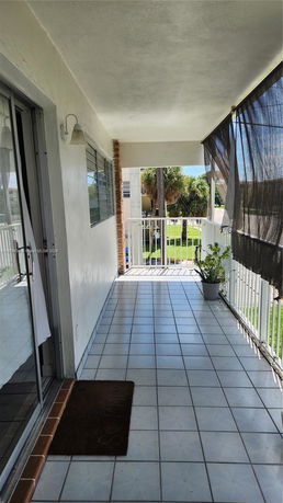 Outdoor balcony with tiled floor and railing, partial view of surroundings.