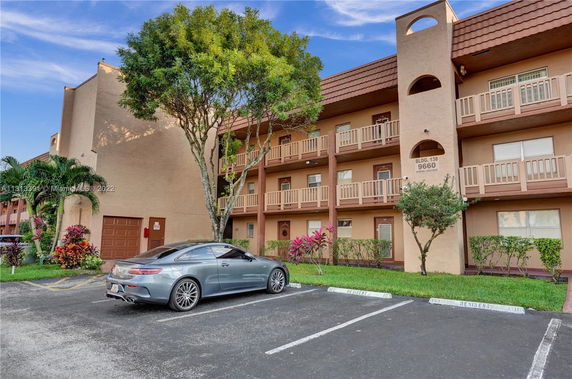 Outdoor parking area with a car in front of a multi-story building with balconies.