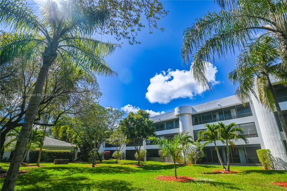 Side view of a multi-story building with balconies surrounded by trees and grass.