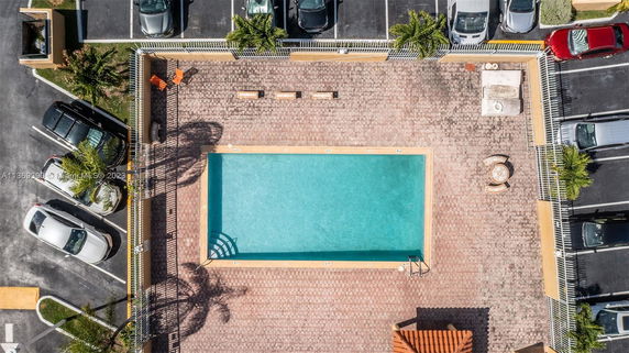 Aerial view of a rectangular swimming pool surrounded by a paved area and adjacent parking spaces.