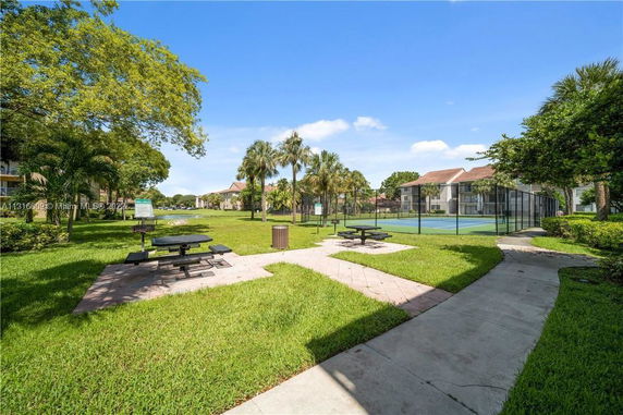 Outdoor area with tennis court and picnic tables surrounded by grass and trees.