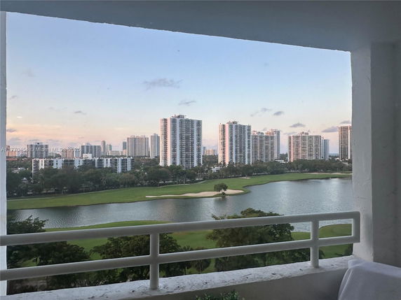 View of tall buildings and a golf course with water from a balcony.