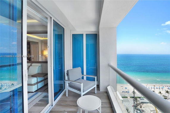 Balcony view overlooking the beach and ocean with outdoor seating and glass railing.