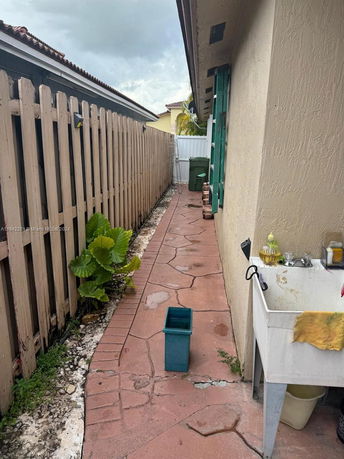 Narrow outdoor space beside a building with a sink, pathway, and fence.
