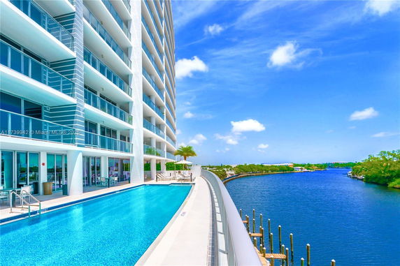 Side view of a multi-story building with an outdoor swimming pool and adjacent waterfront view.