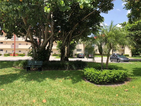 View of a residential building from a green area with trees and a bench.