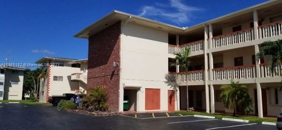 Front view of a multi-story apartment building with balconies and a parking area.