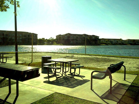 View of apartments near a body of water with picnic tables and benches in the foreground.