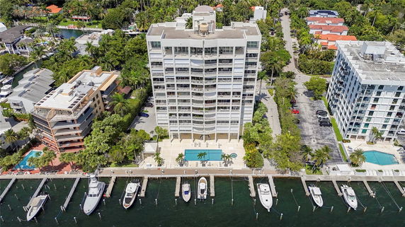 Aerial view of a waterfront residential building with adjacent structures and parked boats.