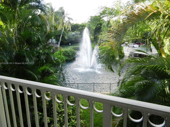 View of a fountain surrounded by lush greenery and palm trees, visible from a balcony with a decorative railing.