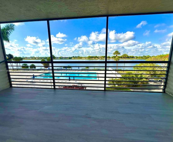 View of a swimming pool and a large body of water with trees and buildings in the background.