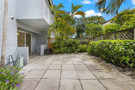 Side view of a house with a patio area surrounded by plants and a fence.