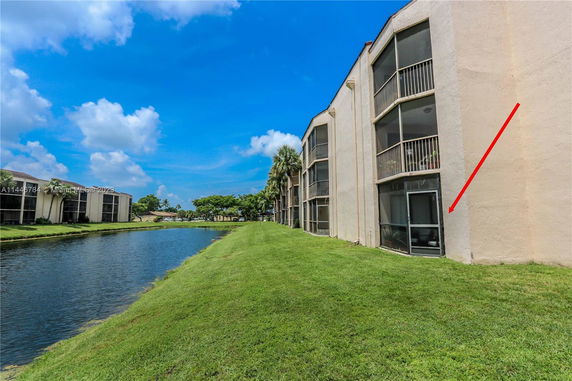 View of a multi-story building beside a waterway with grass and palm trees.