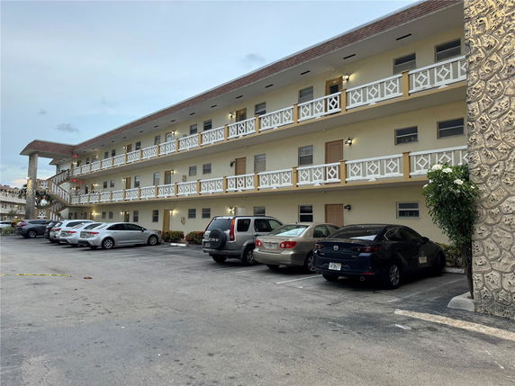 Front view of a three-story residential building with balconies and parked cars.