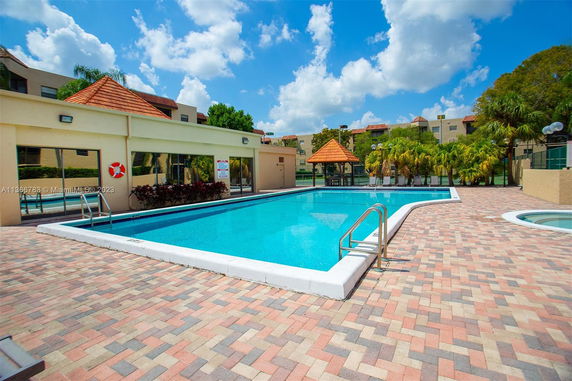 Outdoor swimming pool area with adjacent building and palm trees.