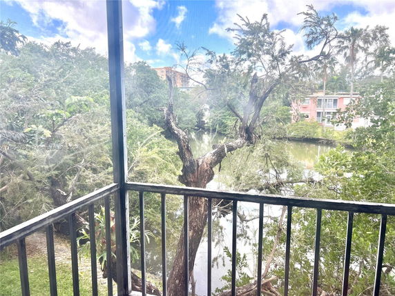 View from a balcony overlooking trees and a water body, with buildings visible in the distance.