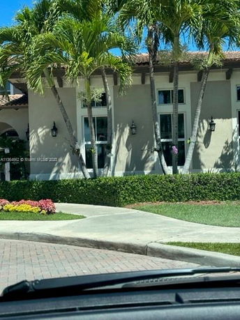 Front view of a house with tall windows and tile roof surrounded by palm trees.