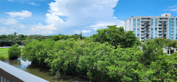 View of a high-rise building with a lush green landscape and waterway in the foreground.