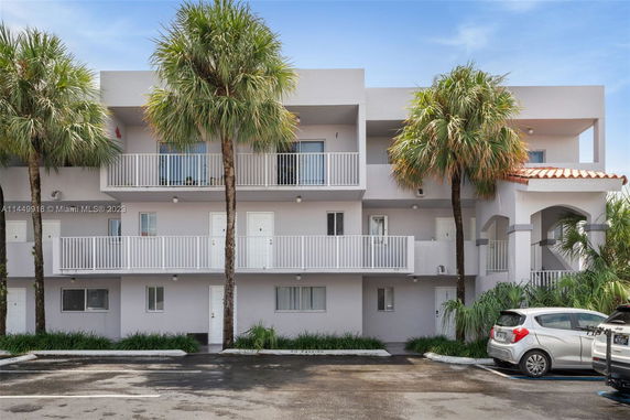 Front view of a multi-story apartment building with balconies and palm trees.