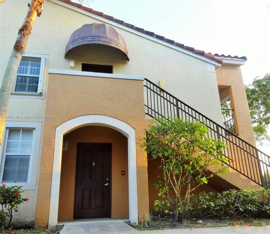 Front view of a two-story building with an external staircase and arched entrance.