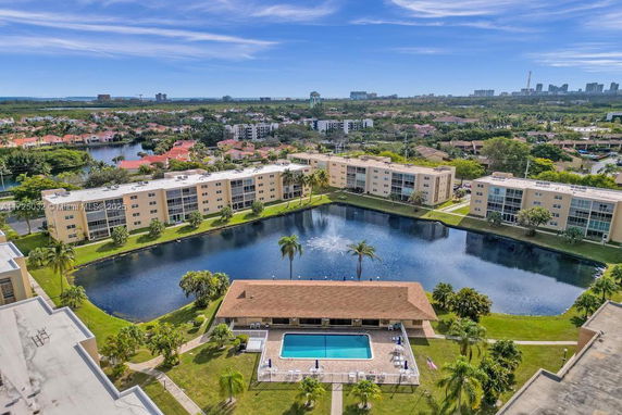 Panoramic view of apartment complexes surrounding a pond with a central water fountain and a swimming pool area in the foreground.