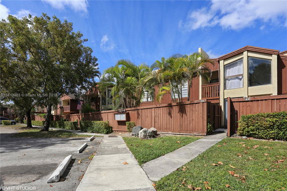Front view of a multi-unit residential building with wooden fencing and landscaping.