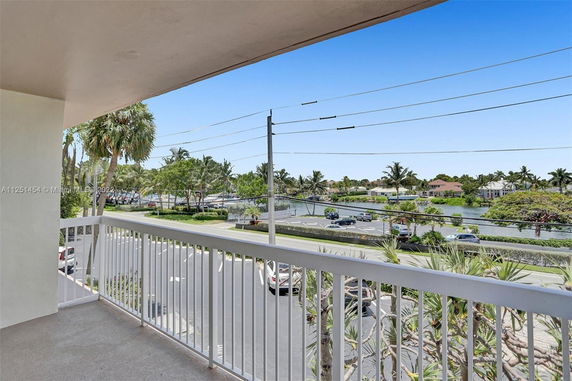 Balcony view overlooking a road, canal, and houses with palm trees.