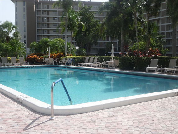 Outdoor swimming pool with lounge chairs and surrounding greenery in front of an apartment building.