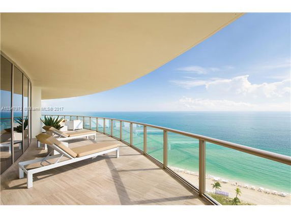 Balcony view overlooking the ocean with lounge chairs and a glass railing.