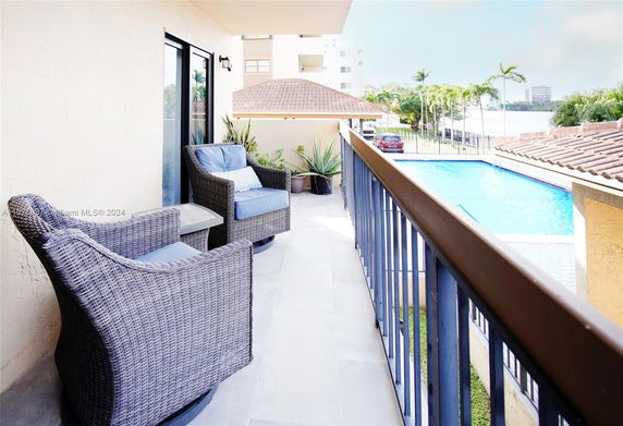 Balcony view with wicker chairs overlooking a pool and surrounding area.