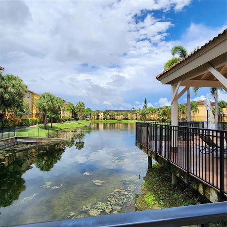 View of buildings by a pond with palm trees and sky reflections.