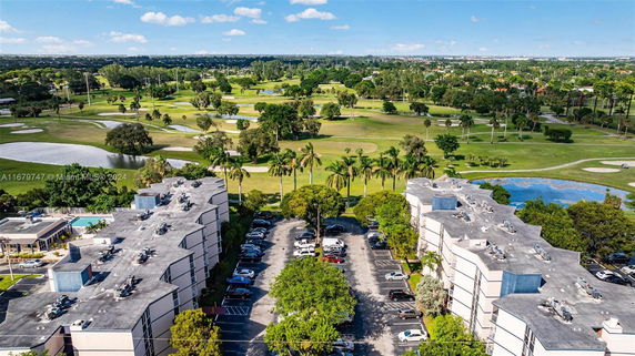 Aerial view of a residential complex with parking area and green landscape surrounding it.
