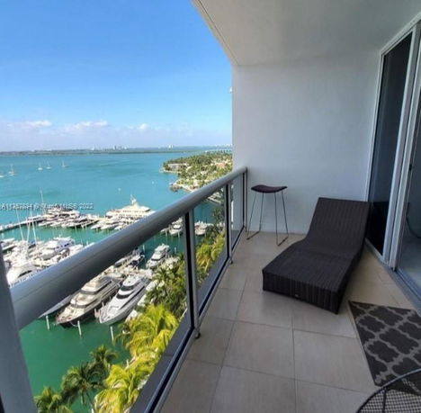 A balcony with a lounge chair offering a panoramic view of a marina and waterfront area.