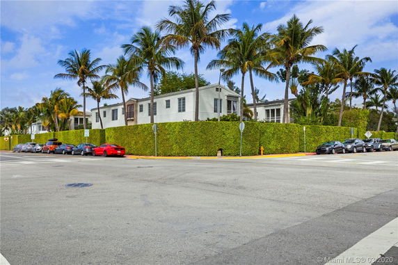 Front view of a multi-story building with tall palm trees and a hedge.